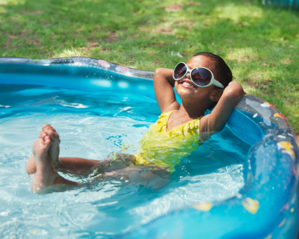 Young girl lounging in a kiddie pool with sunglasses on her face.
