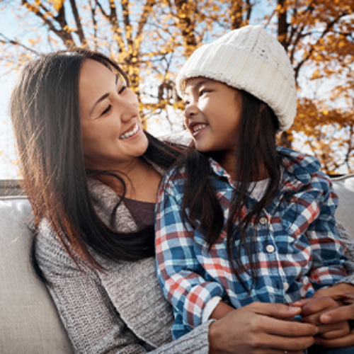 Woman and her daughter smiling outdoors.