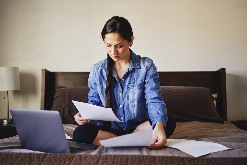 Woman sitting on a bed looking at papers.