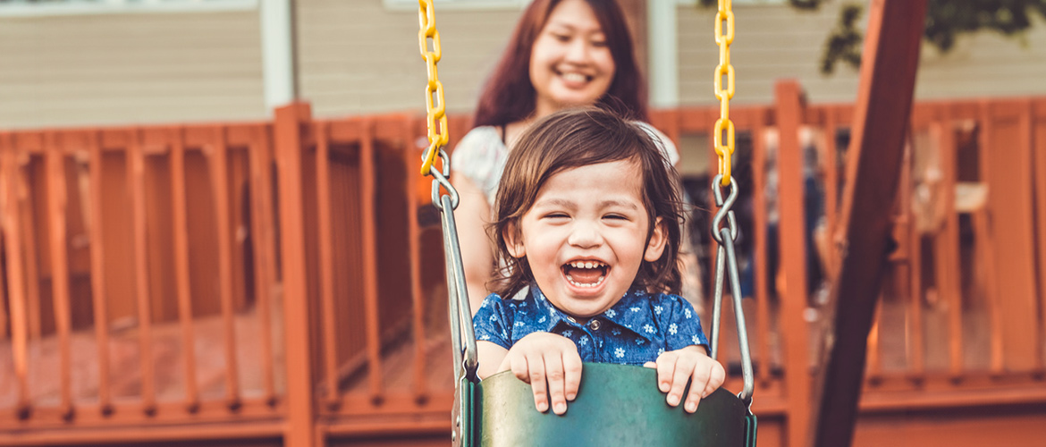 Woman stands behind child sitting in a swing