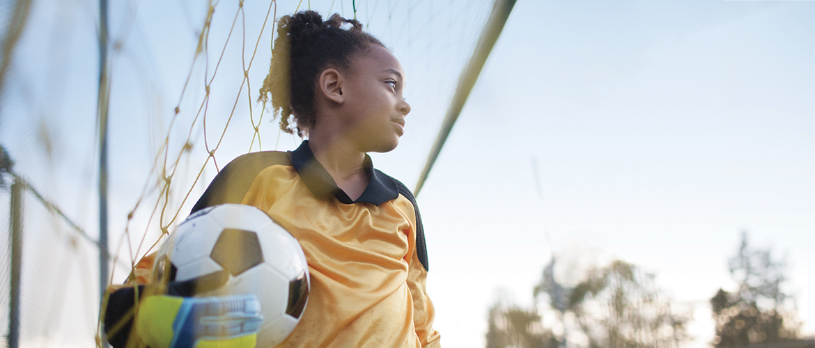 Girl holds a soccer ball as she stands in front of a goal