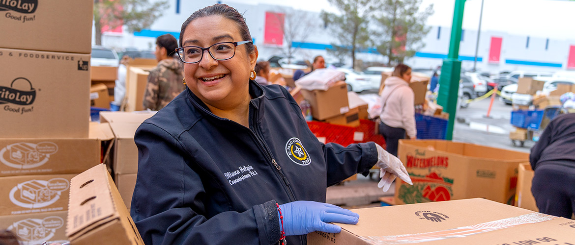 Woman smiles as she opens cardboard box filled with food to distribute