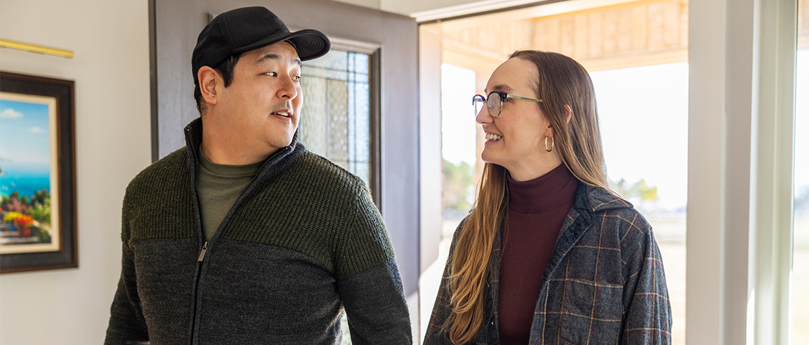 Man in black hat and woman in glasses walk through the front door of house