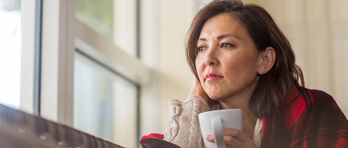 Woman with coffee mug looks out the window from her living room
