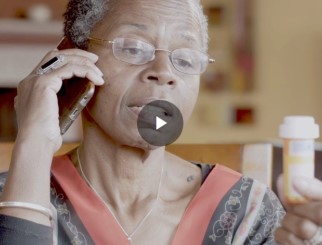 Mujer mayor canosa hablando por su teléfono móvil mientras mira un frasco de medicamentos, como si estuviera revisando sus medicamentos con un farmacéutico o médico.