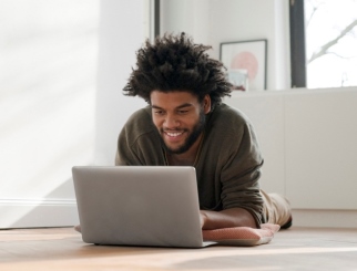 Young man laying on the floor with his laptop and smiling. 