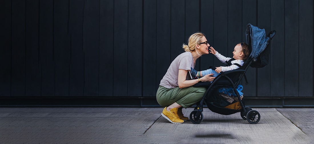 Mother crouching in front of her child in a stroller as the child reaches out for her.