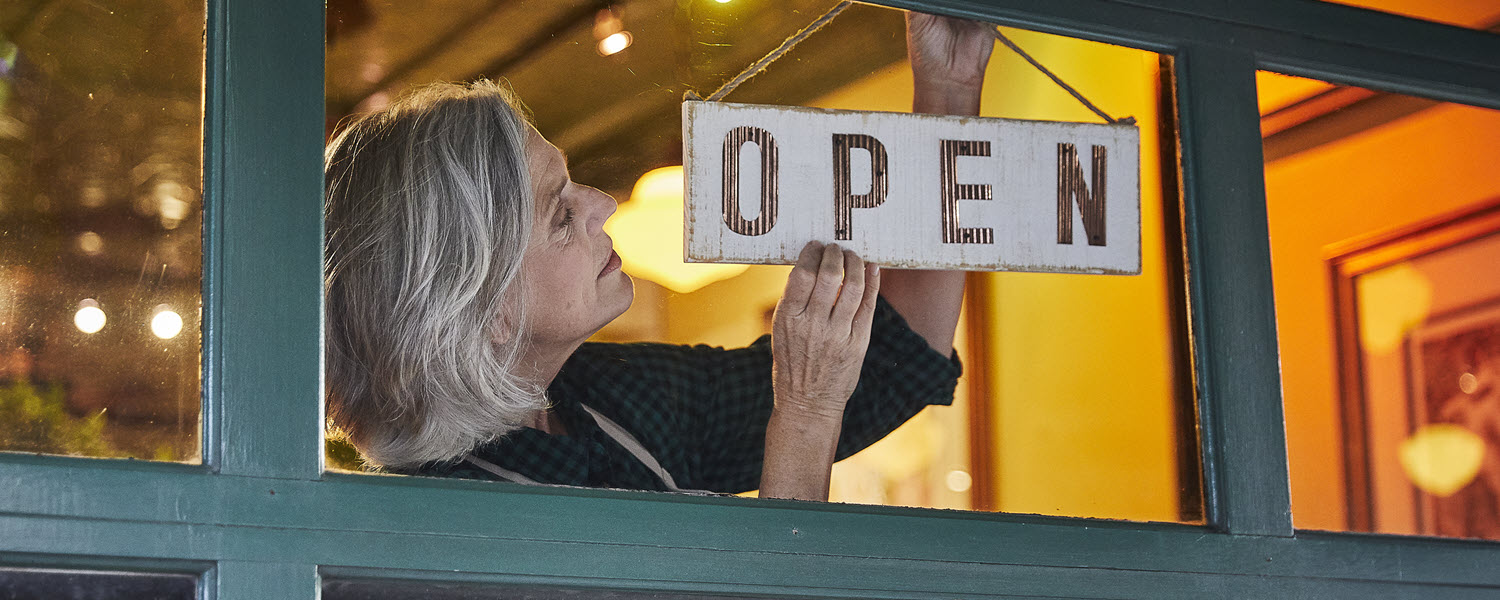 Small business owner hanging open sign on window