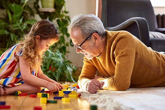 Grandfather and granddaughter play with Legos on the floor 