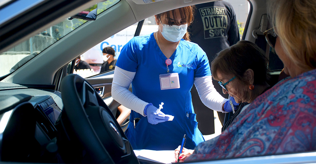 Una trabajadora de atención médica aplica un vacuna en un evento de vacunación sin bajar del auto