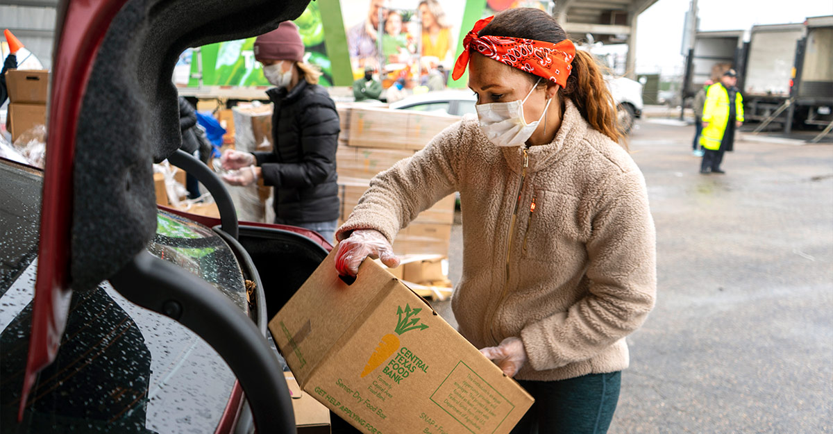 Un socio comunitario carga una caja de comida en el baúl de un automóvil en un banco de alimentos