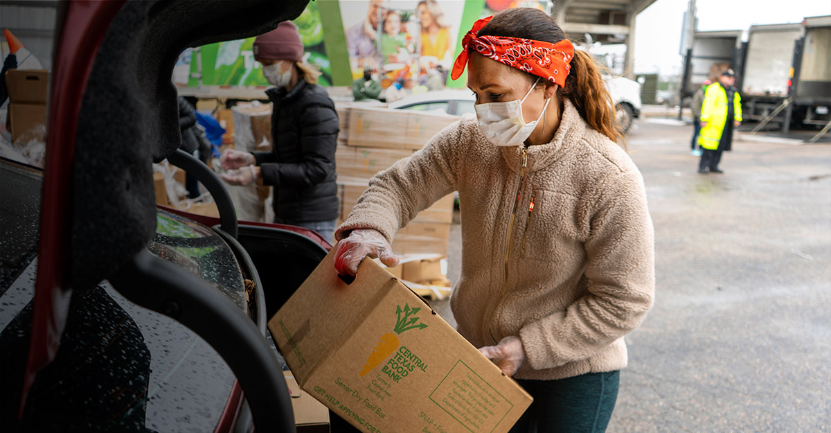 Una socia comunitaria carga una caja de comida al baúl del auto en el banco de alimentos