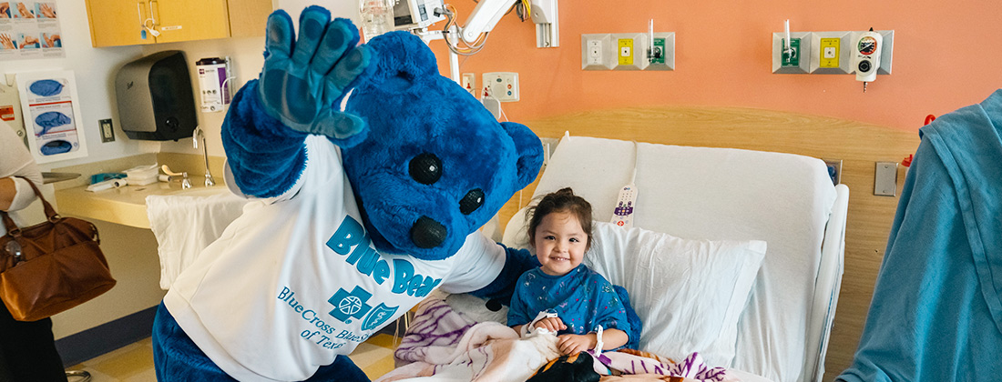 BCBSTX mascot Blue Bear visits a young girl in a hospital bed. 