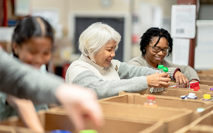 Three people fill food boxes to be donated. 