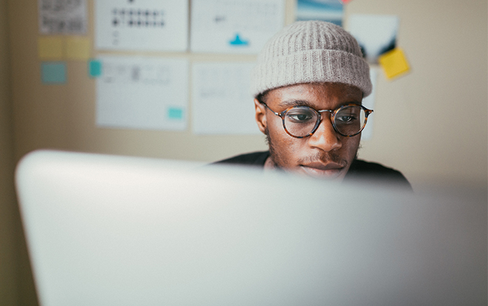 Black man a wearing beanie in an office looks at a computer intently.