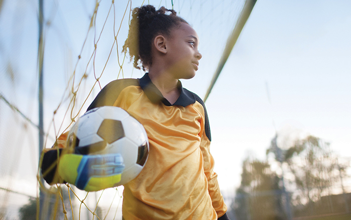 Young soccer player holding ball near goal net