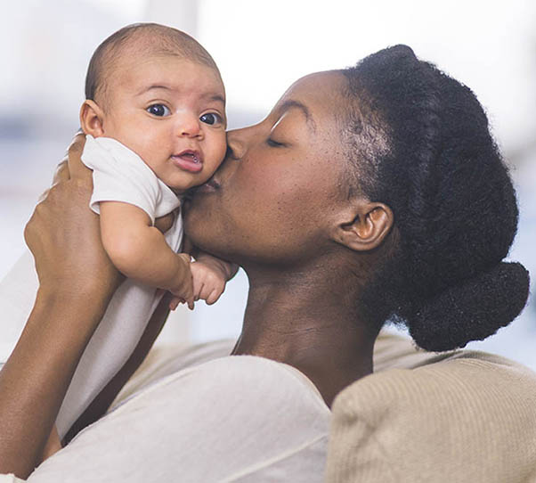 Young African American woman kisses infant child