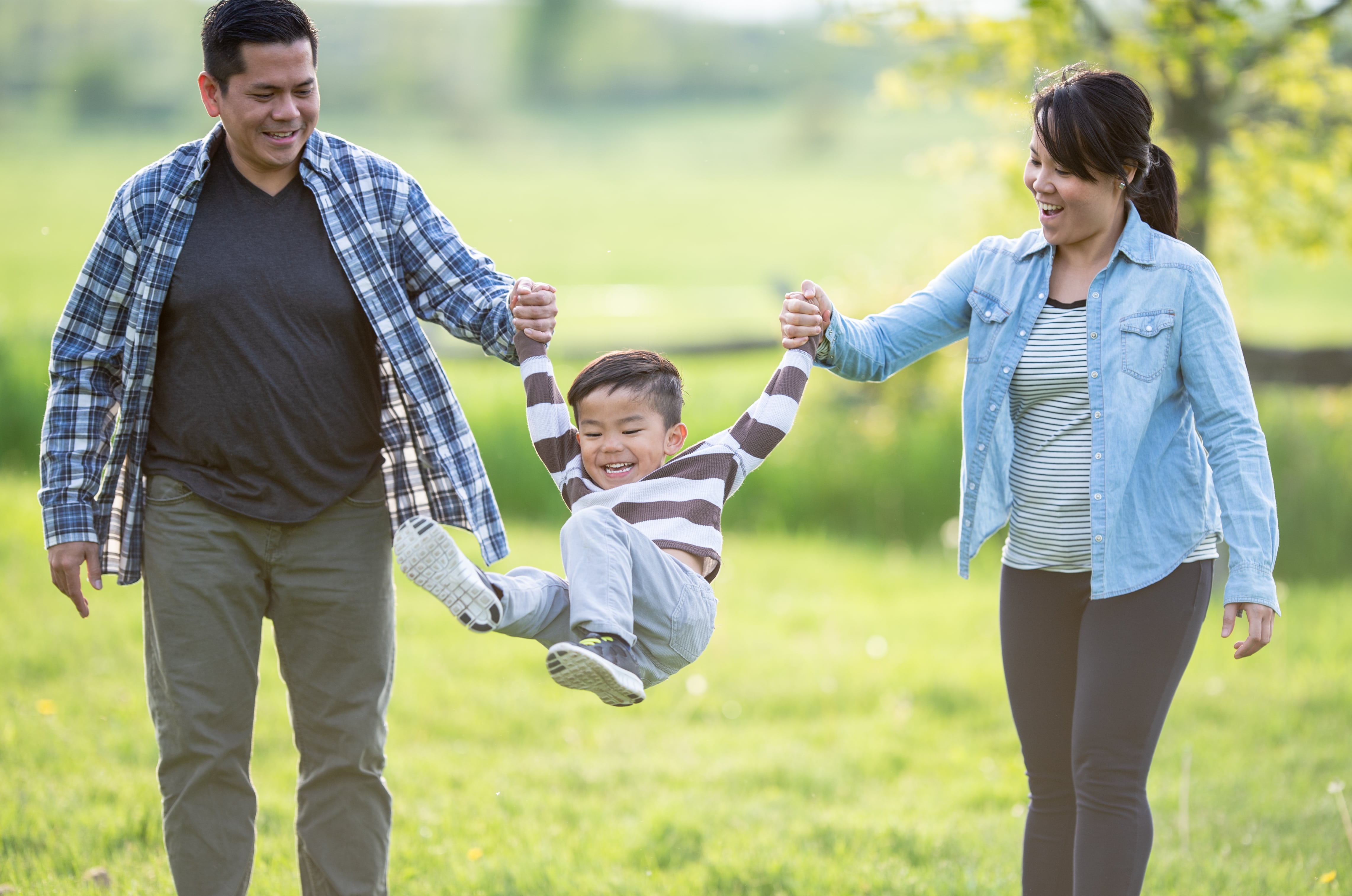 Man and woman holding the hands of their smiling son and swinging him