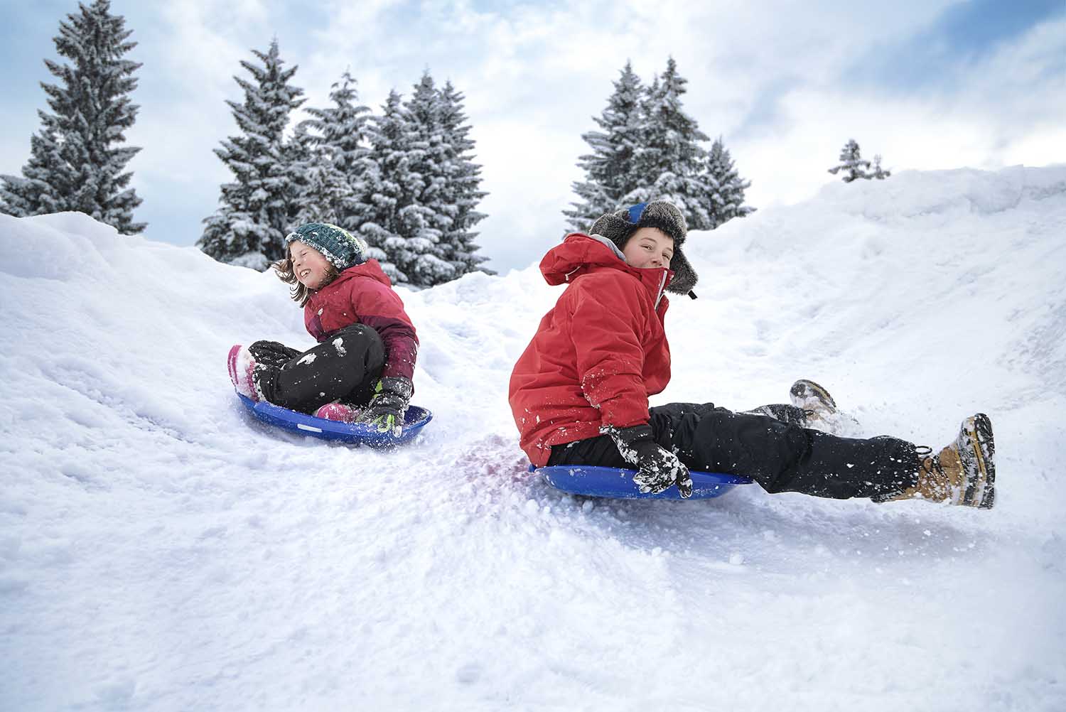 Un niño y una niña bajando en deslizador por una colina nevada