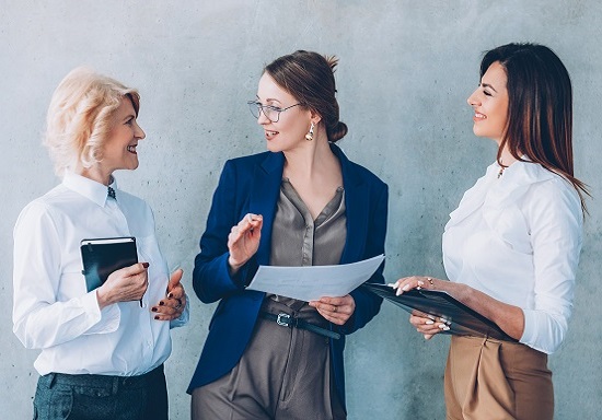 Three business women in suits discussing project and holding portfolios.