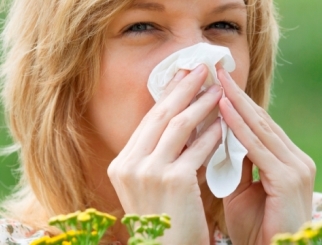 Close-up of a blonde Caucasian woman blowing her nose with a tissue.