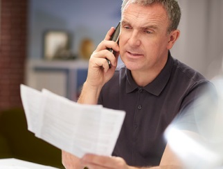 Caucasian man holding bills in his left hand and holding a phone up to his ear with his right hand.